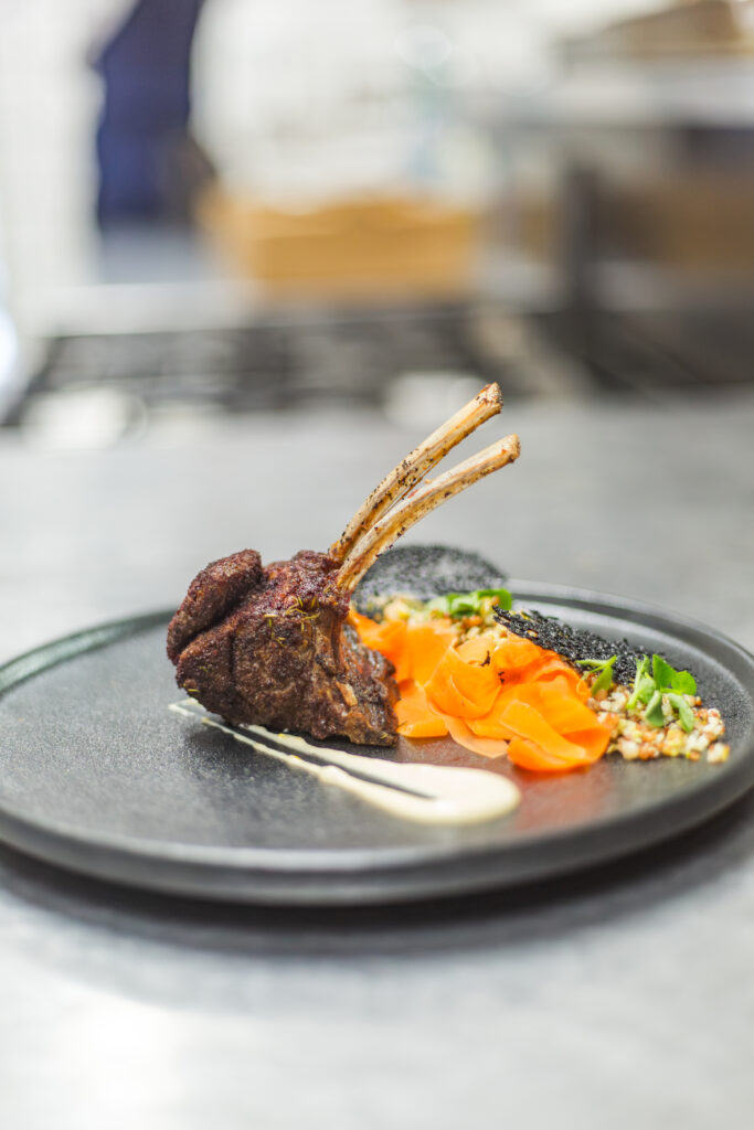 A gourmet plated lamb chop dish with elegant carrot garnishes prepared by chefs for a fine dining event.
