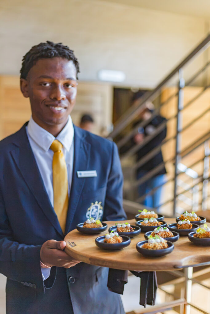 A hospitality student presenting a beautifully plated fine dining culinary platter at the 2026 Tshwane GMS Hospitality Soiree.