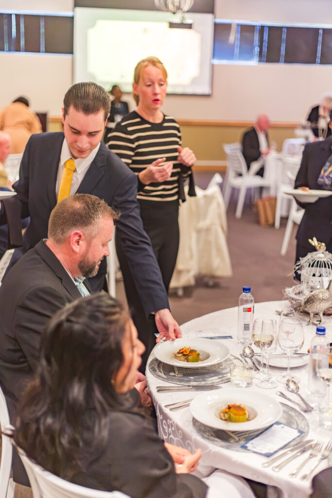CHS front-of-house hospitality students serving beautifully plated dishes to corporate guests at a formal banquet.