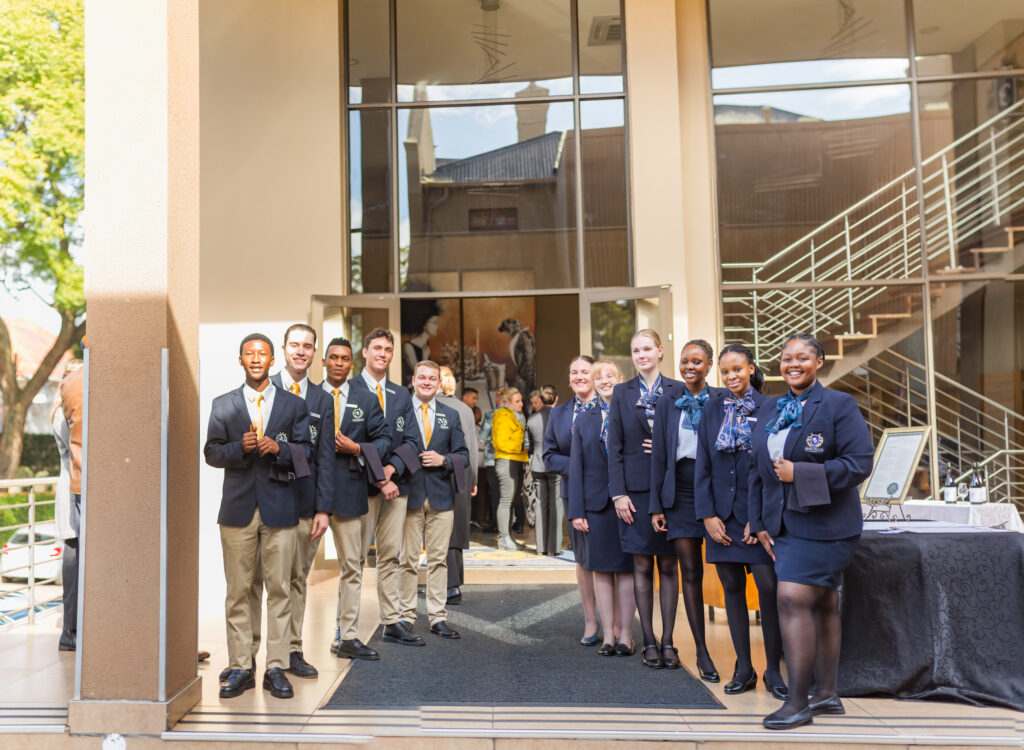 A group photo of Capital Hotel School students in formal uniform standing outside the event venue entrance.