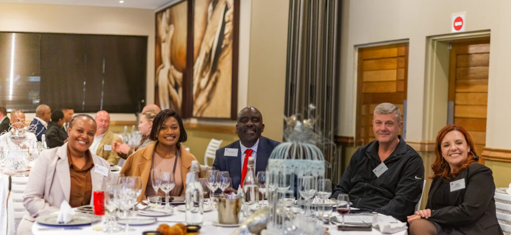 Smiling hospitality professionals and industry executives seated together at a beautifully decorated event table.