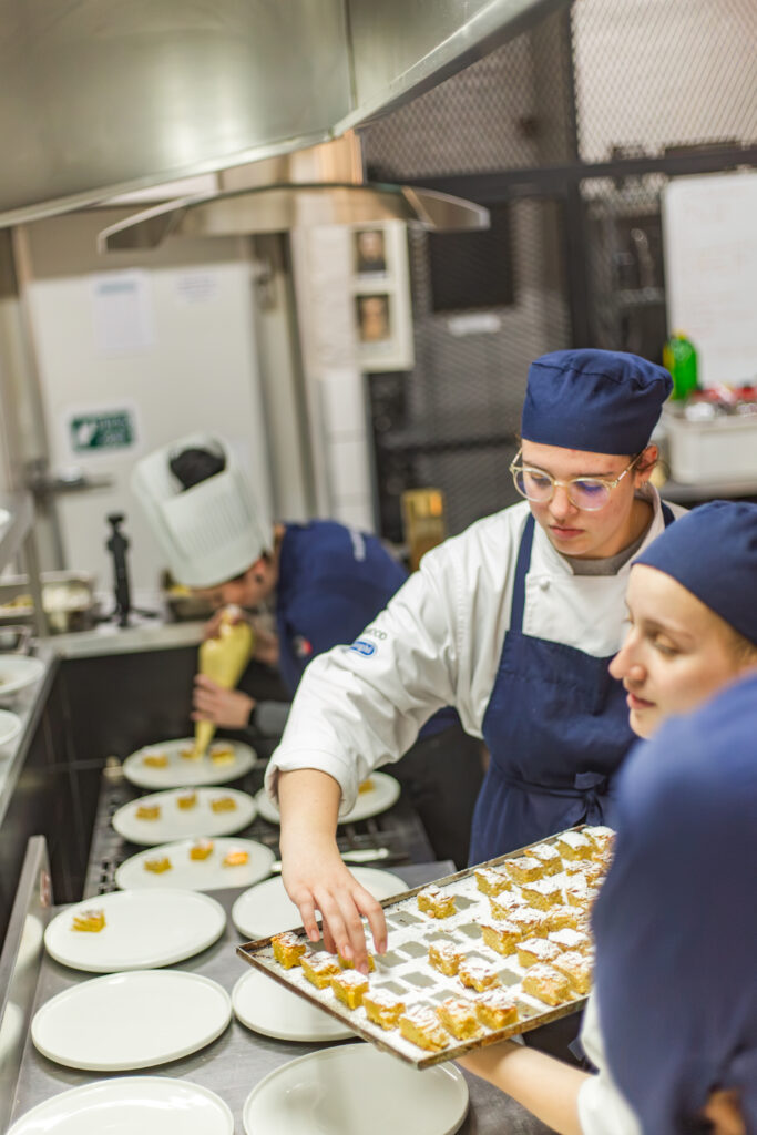 Capital Hotel School culinary arts students working together to plate and dust sweet pastries with powdered sugar in a training kitchen.